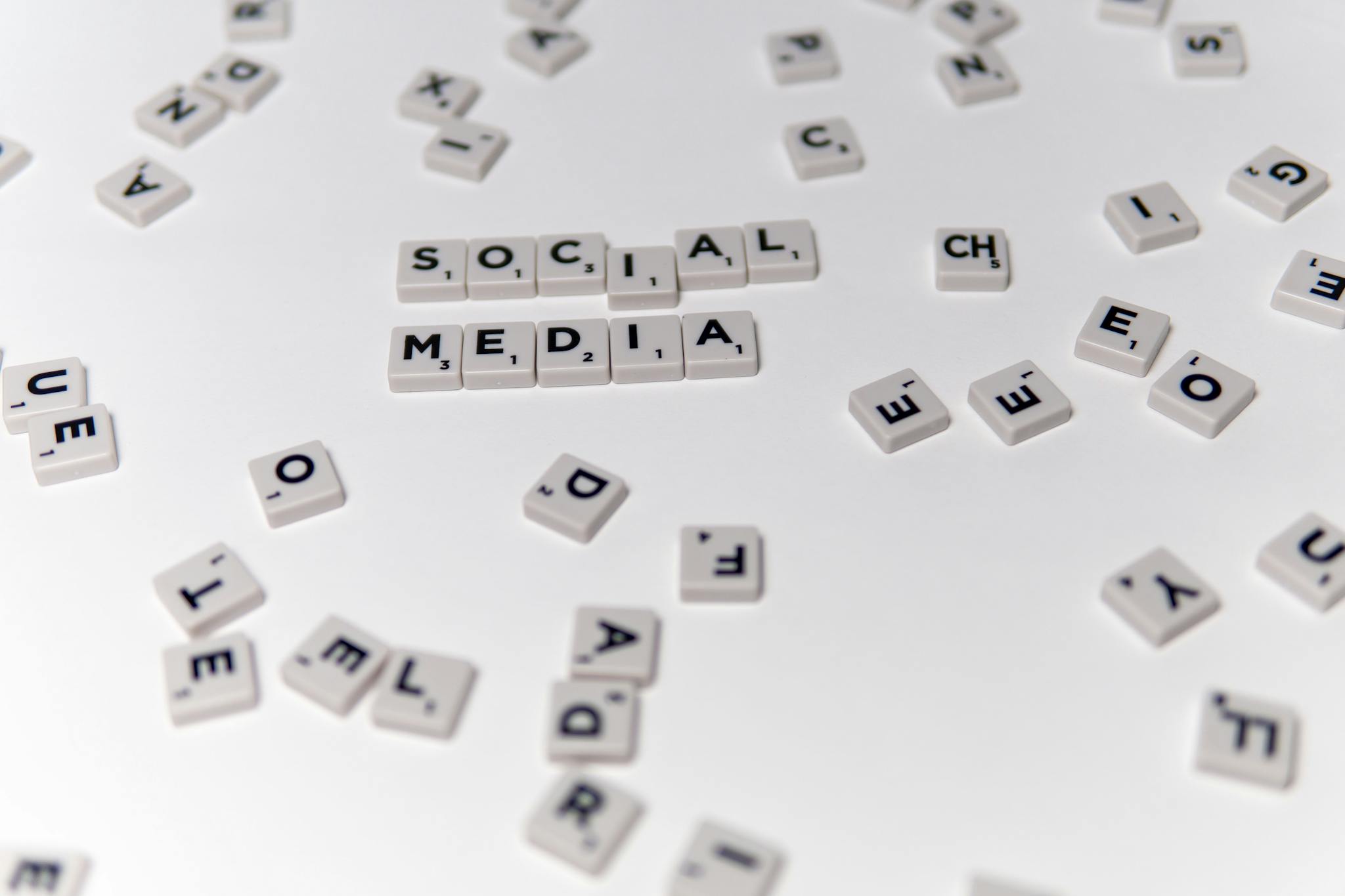 White Scrabble tiles forming the phrase 'social media' on a scattered background.